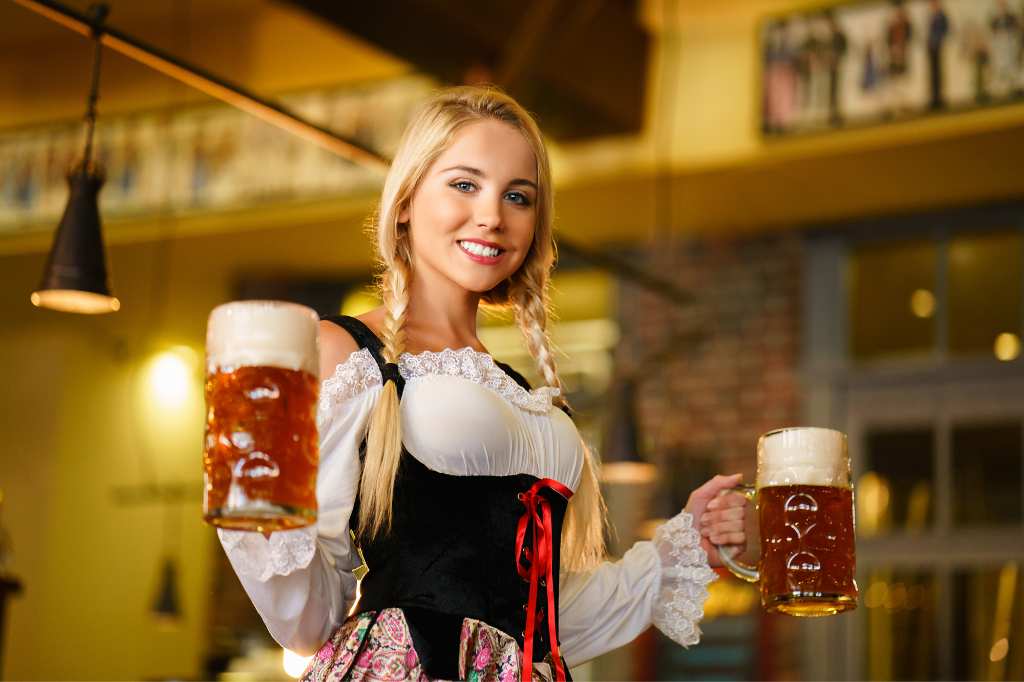 Sonriente chica rubia alemana lleva cerveza en el festival Oktoberfest en Mallorca