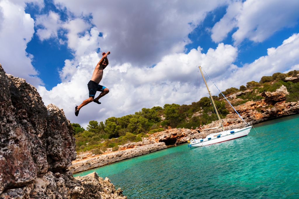 El hombre saltando de acantilados en la soleada Cala Sa Nau, Mallorca